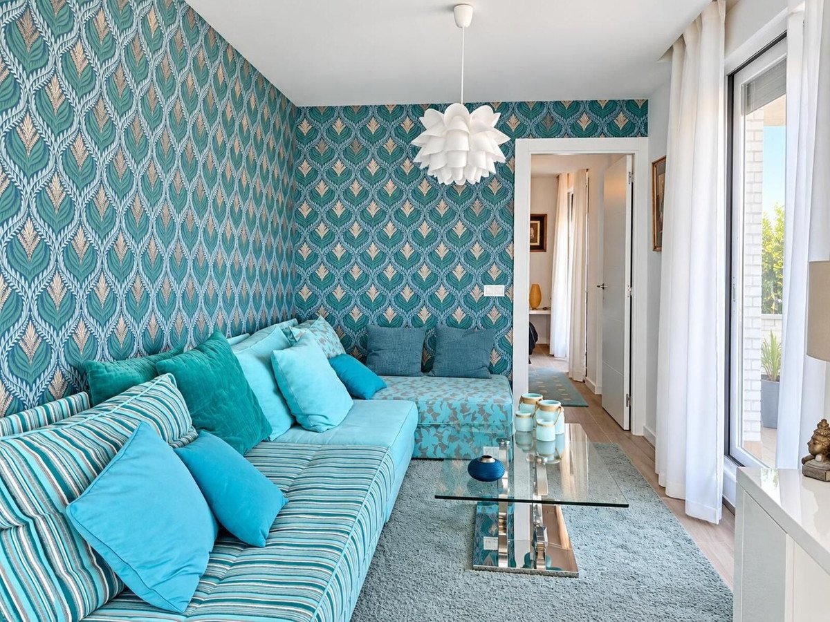 Modern living room with teal patterned wallpaper, a sectional sofa with blue and teal cushions, and a glass coffee table.