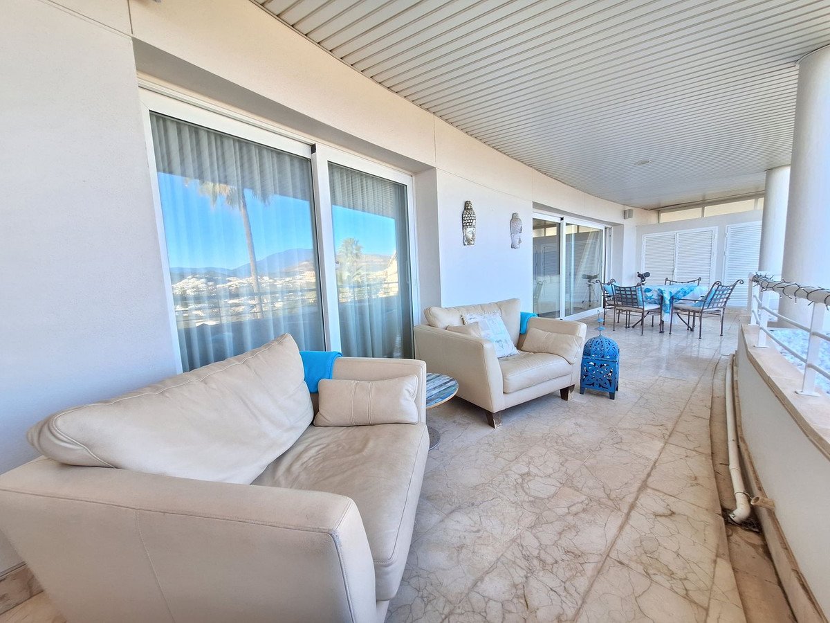 Spacious terrace with comfortable sofas, a dining set, and a view of the sea and hills.