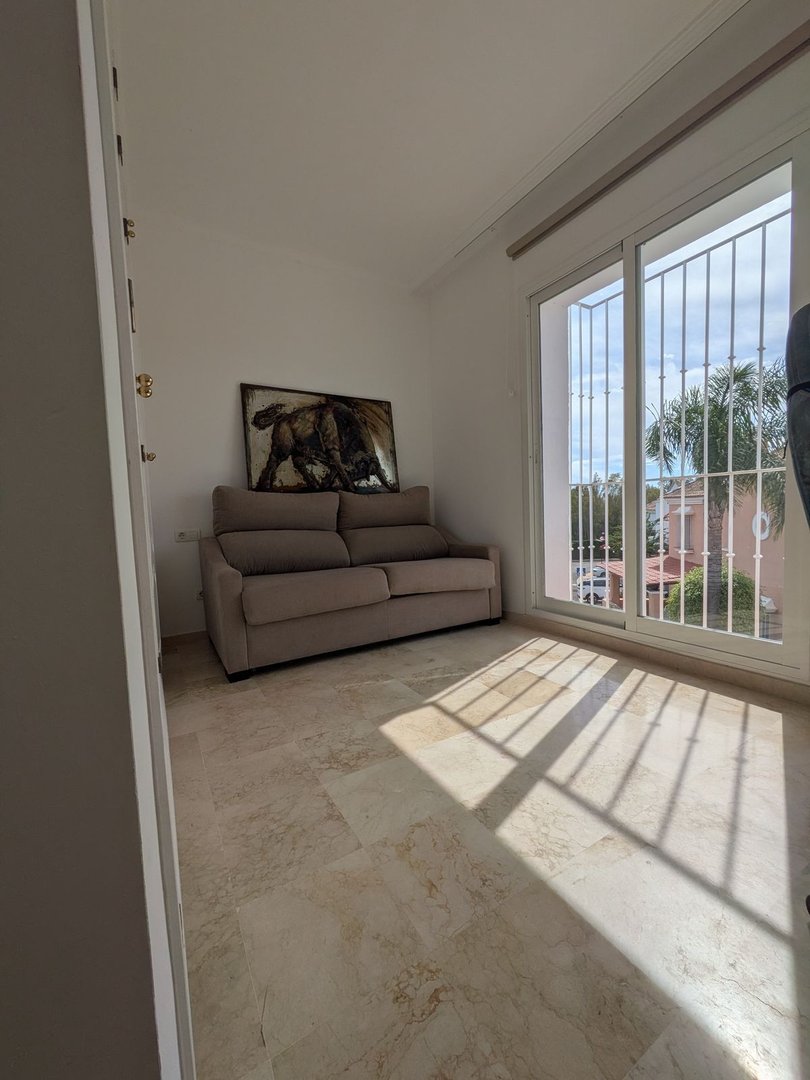 Cozy living area with a sofa and artwork, featuring a large window with a view of palm trees and buildings.