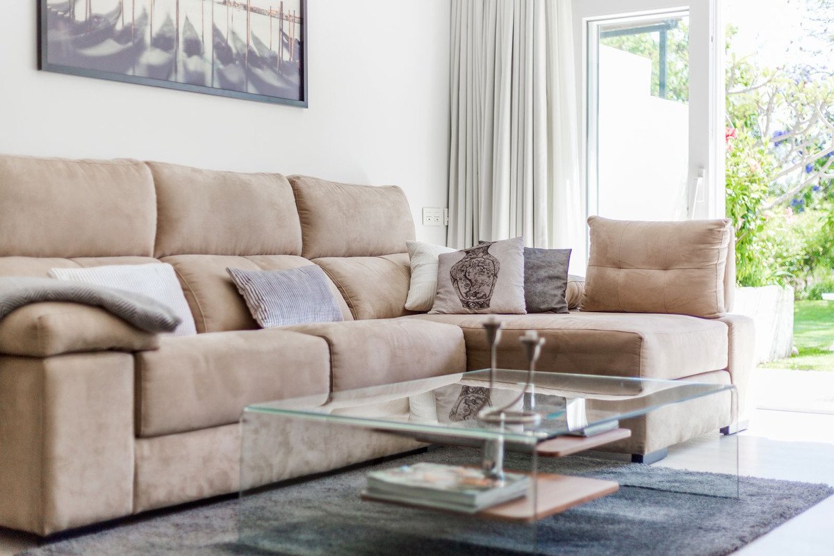 Beige sectional sofa in bright living room with glass coffee table and garden view