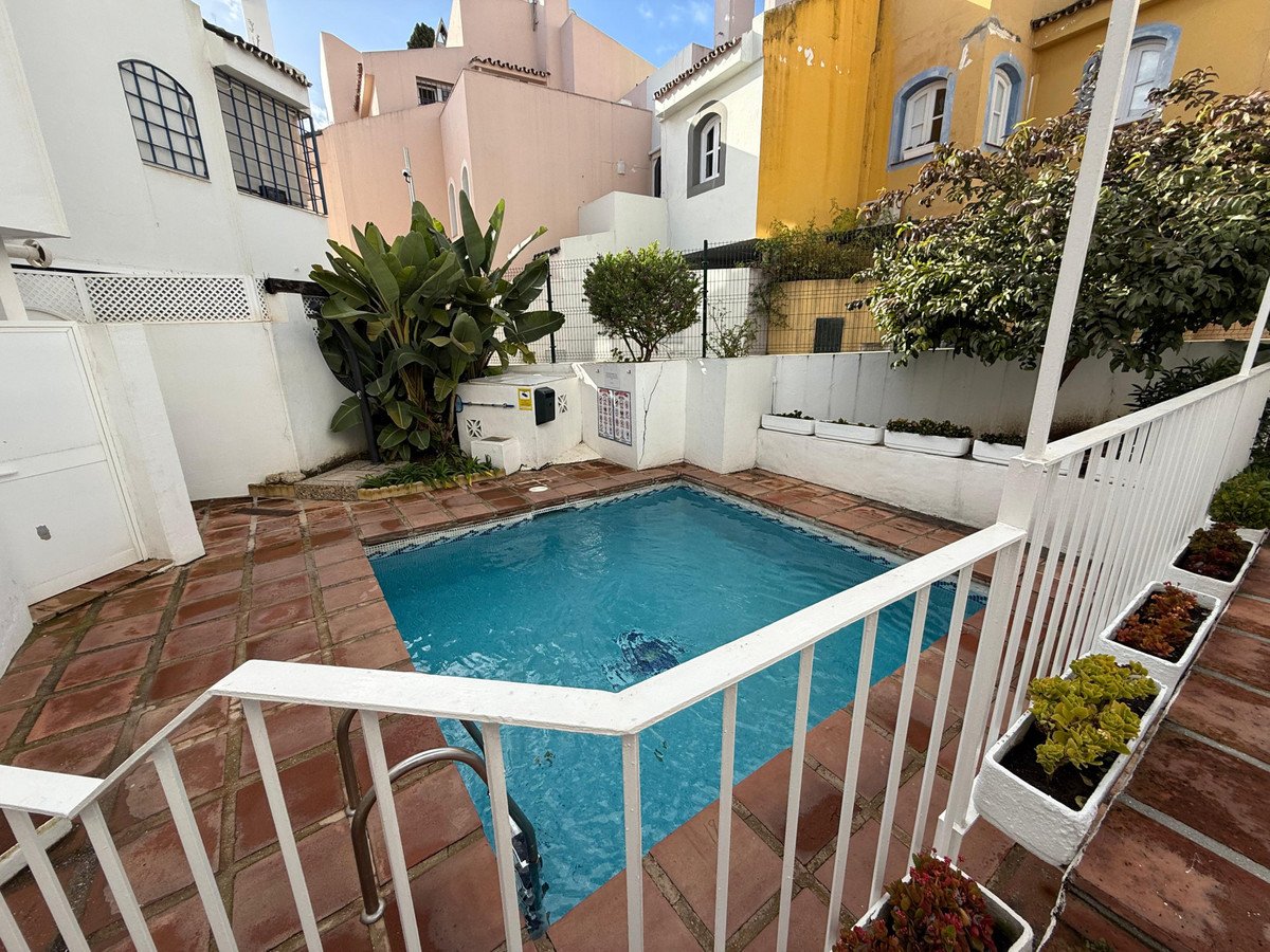 A private swimming pool with blue water and terracotta tiling, surrounded by white walls and lush greenery. Includes a white railing and steps.