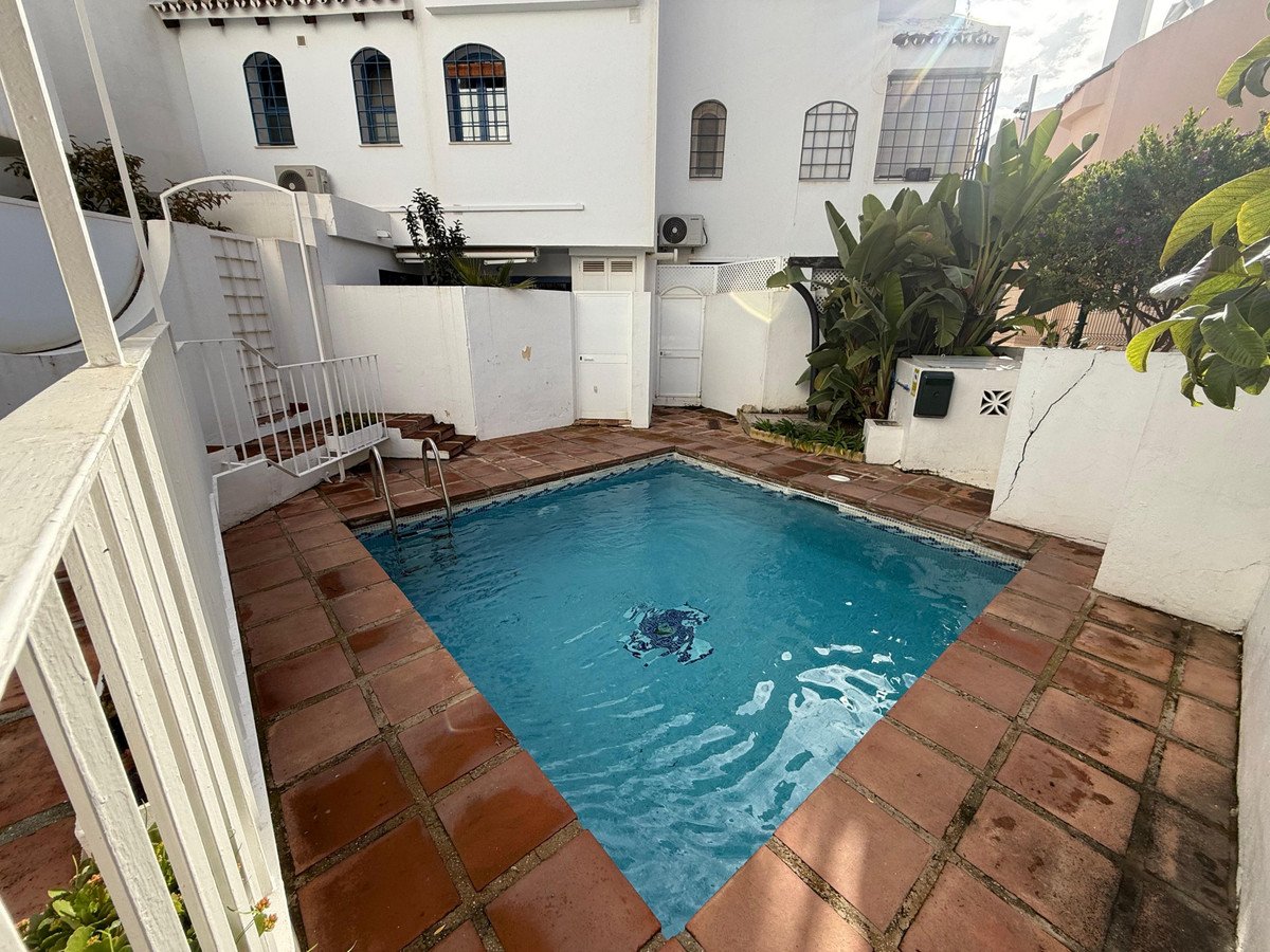 A private swimming pool with tiled surround, surrounded by white walls, lush greenery, and steps leading down.