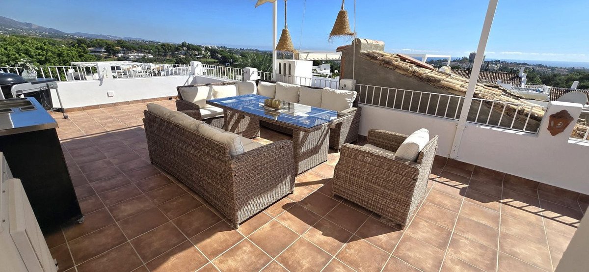 Rooftop terrace with wicker seating, glass table, and panoramic mountain and city views