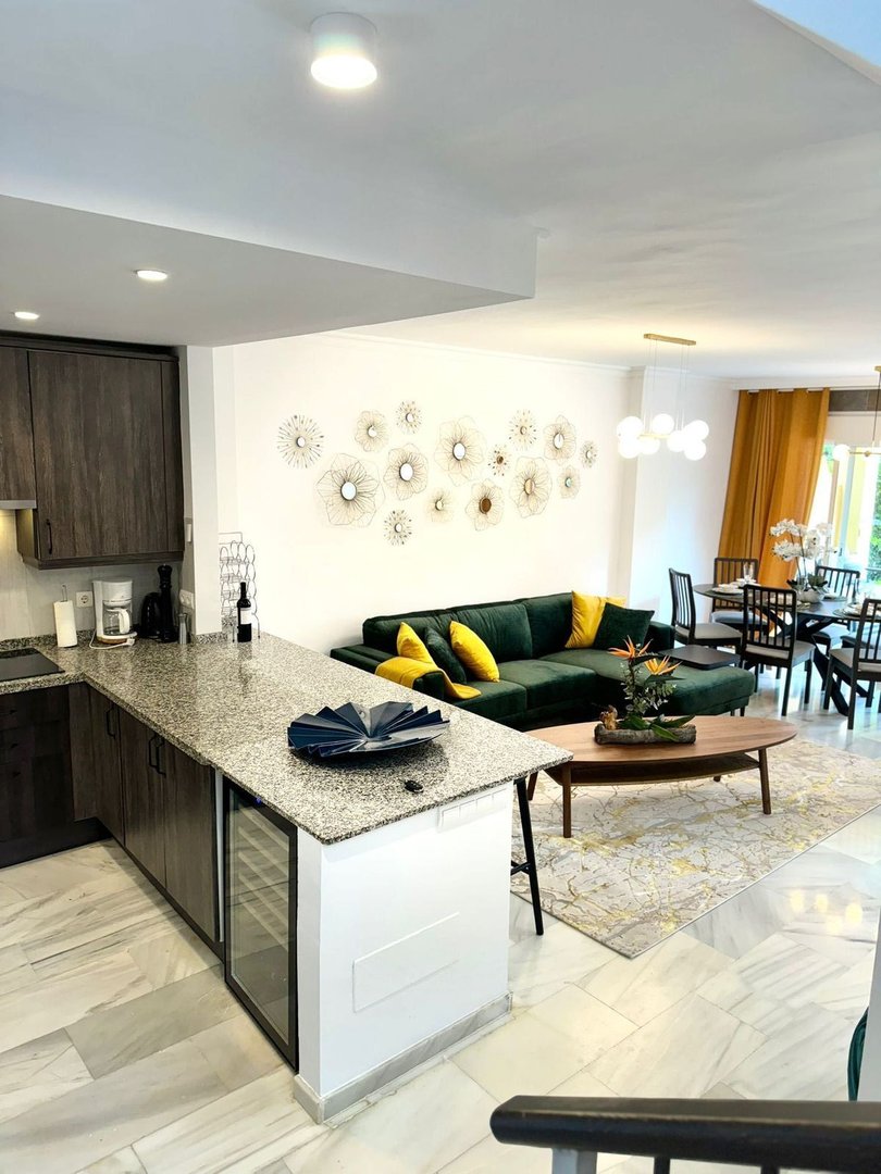 Modern living and dining area with a green sectional sofa, granite island, and elegant wall decor.
