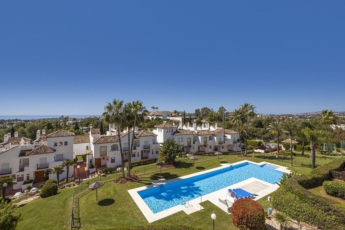 White apartment complex with a swimming pool and palm trees under a clear blue sky