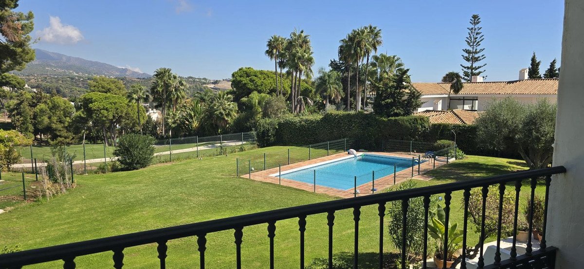 A swimming pool and a manicured lawn are visible with palm trees and mountains in the background.