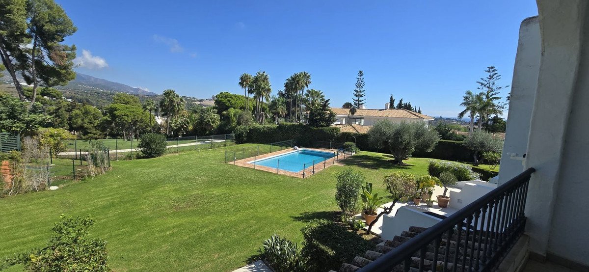 A view of a private swimming pool surrounded by a lush green garden and palm trees, with mountains in the background.