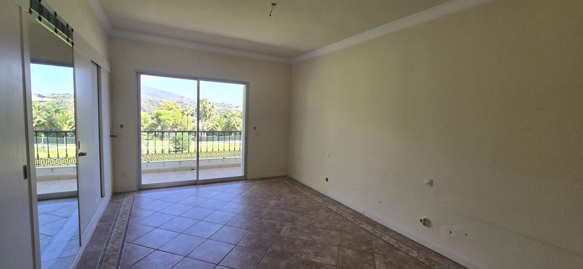 Empty bedroom with a sliding glass door leading to a balcony overlooking palm trees and mountains. Features a wardrobe with mirrored doors.