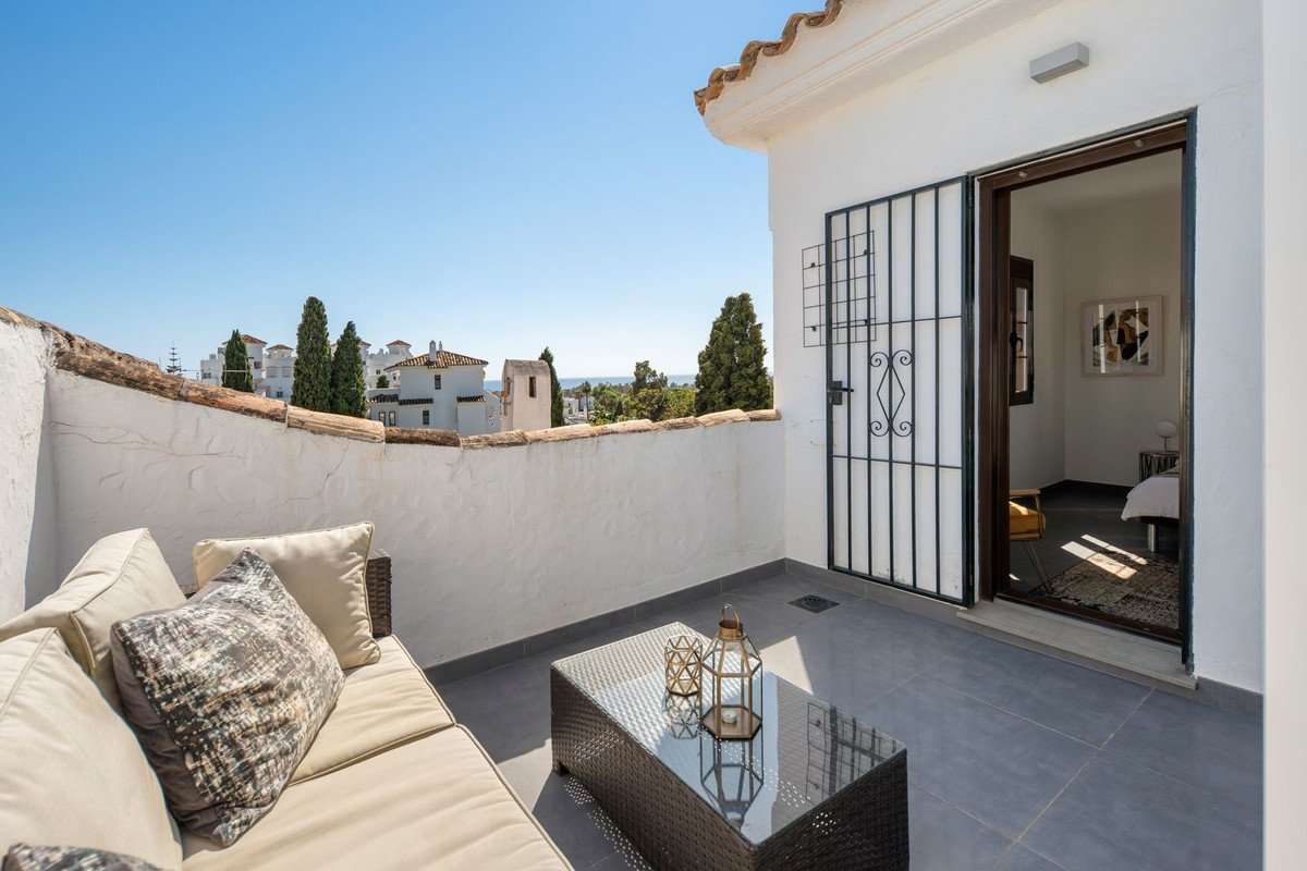 A furnished terrace with comfortable seating and a coffee table, overlooking rooftops and the distant sea.