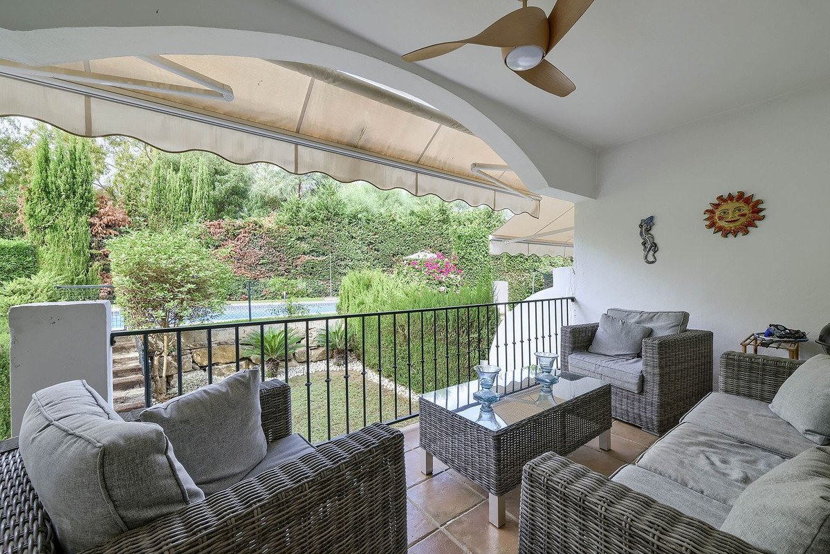 Covered patio with wicker furniture overlooking a garden and pool