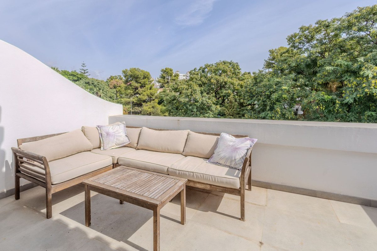 Outdoor terrace with beige seating, wooden table, and green tree view