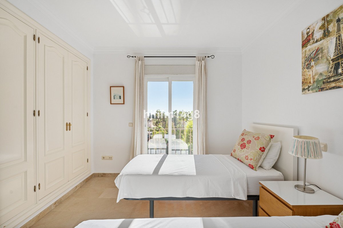 A bright bedroom with two single beds, large wardrobe, and a sliding door leading to a balcony with a green view.