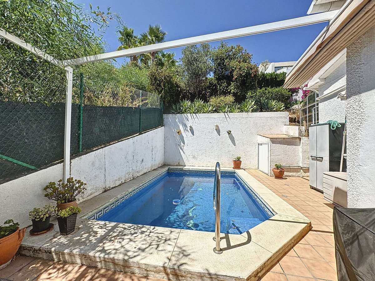 A private swimming pool with a tiled surround, surrounded by potted plants and a sunny terrace.