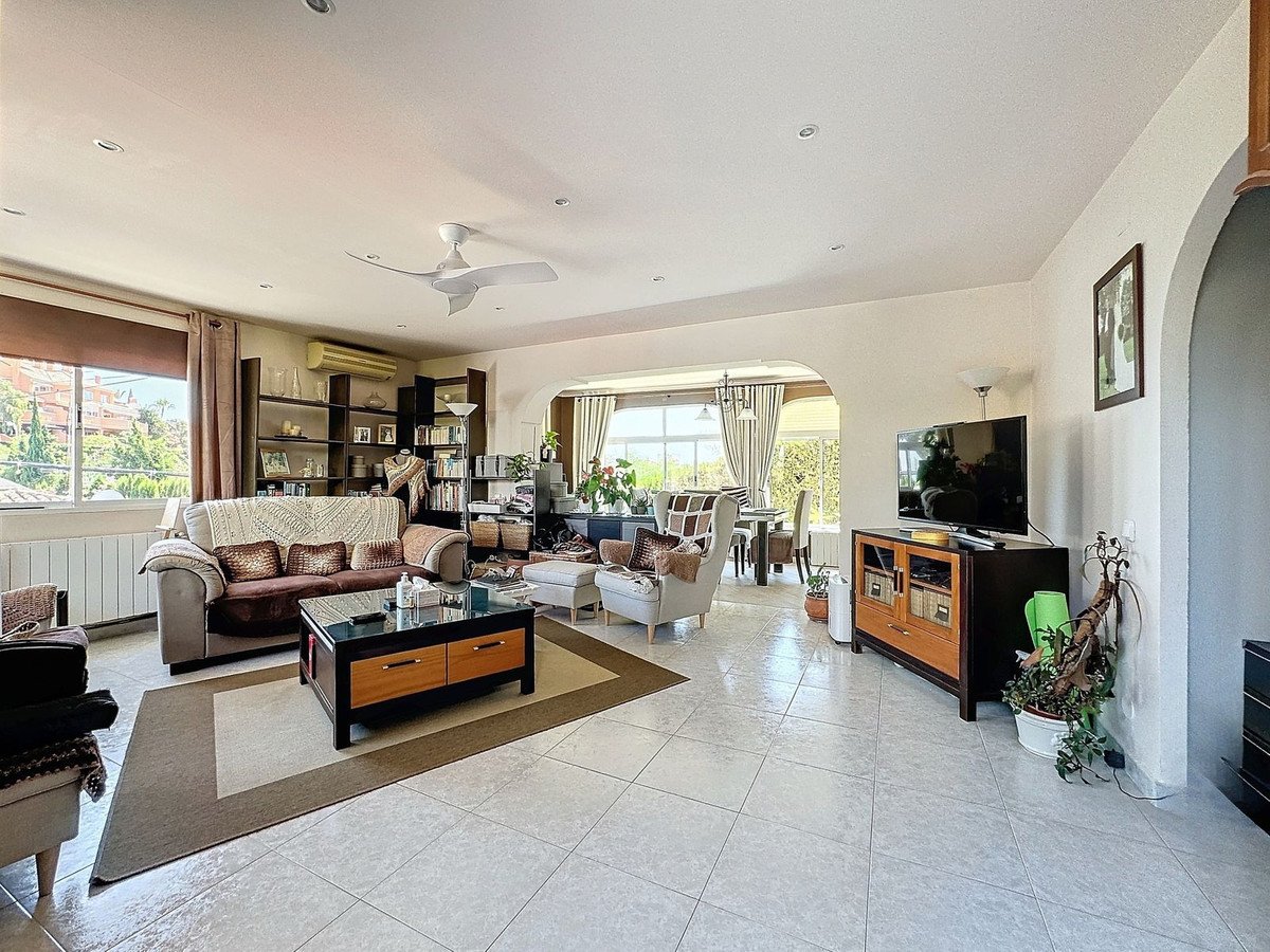 Spacious living room with comfortable sofa, coffee table, television, and view of greenery through the windows.