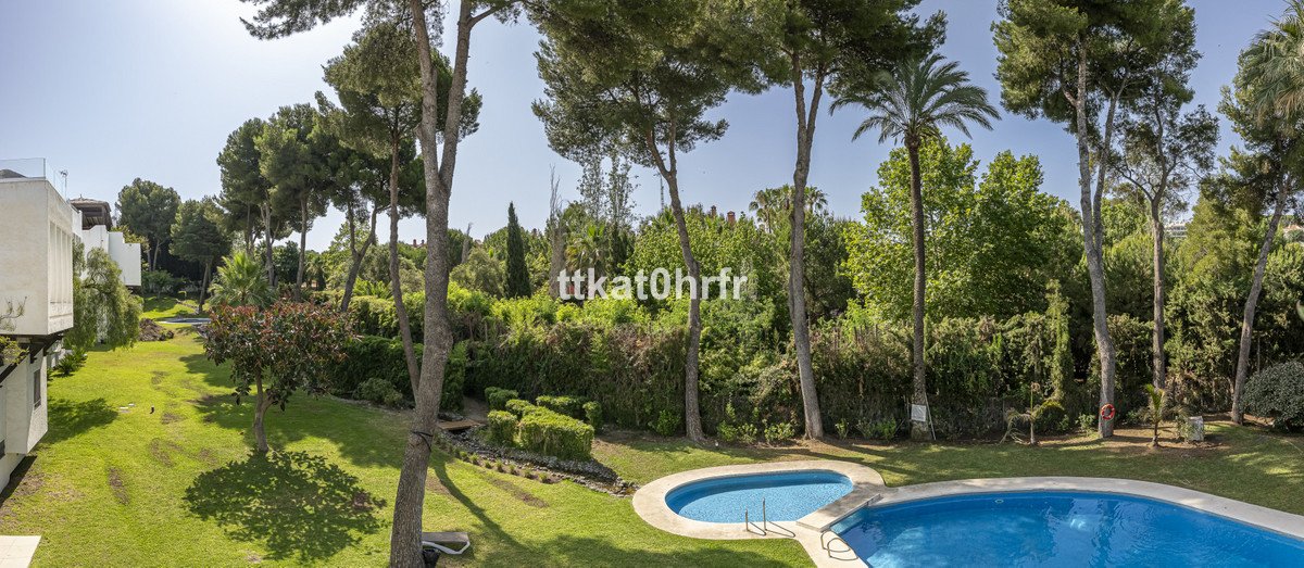 A well-maintained garden with a swimming pool, lush trees, and manicured bushes surrounds the property.