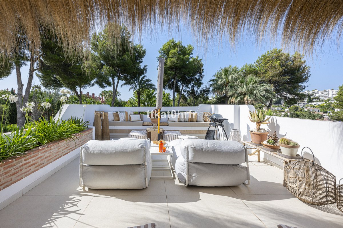A spacious terrace with comfortable seating, built-in benches, plants, and a barbecue, offering a scenic view.