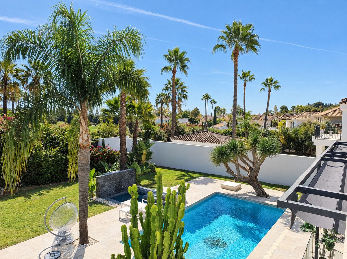 Spacious backyard with a swimming pool, lush green garden, palm trees, and a terrace with outdoor seating.