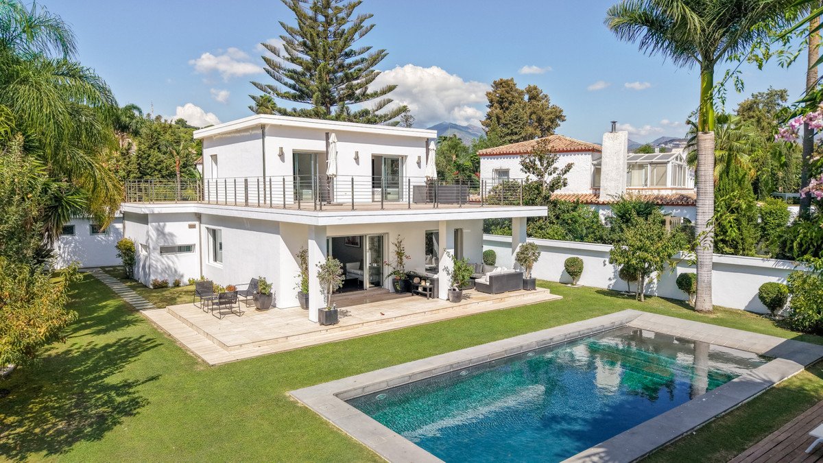 Modern villa with a swimming pool, multiple terraces, and lush green gardens with mountain views in the background.
