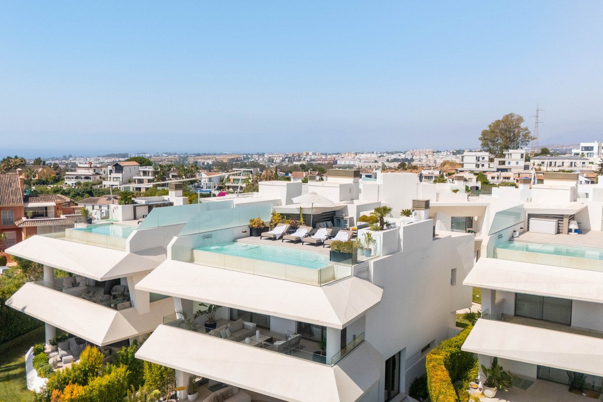 Modern penthouse with rooftop infinity pool, lounge chairs, and panoramic views of a coastal town under a clear blue sky.