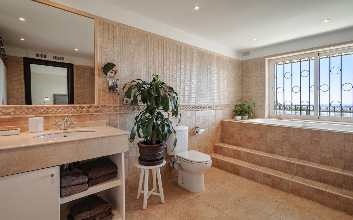 Spacious bathroom with a built-in bathtub, a sink, toilet, and a large window overlooking the ocean.