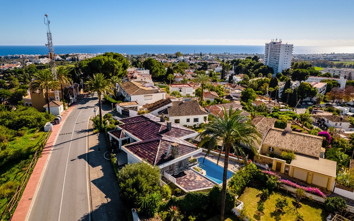 Aerial view of a white villa with a swimming pool and garden, overlooking the sea and town.