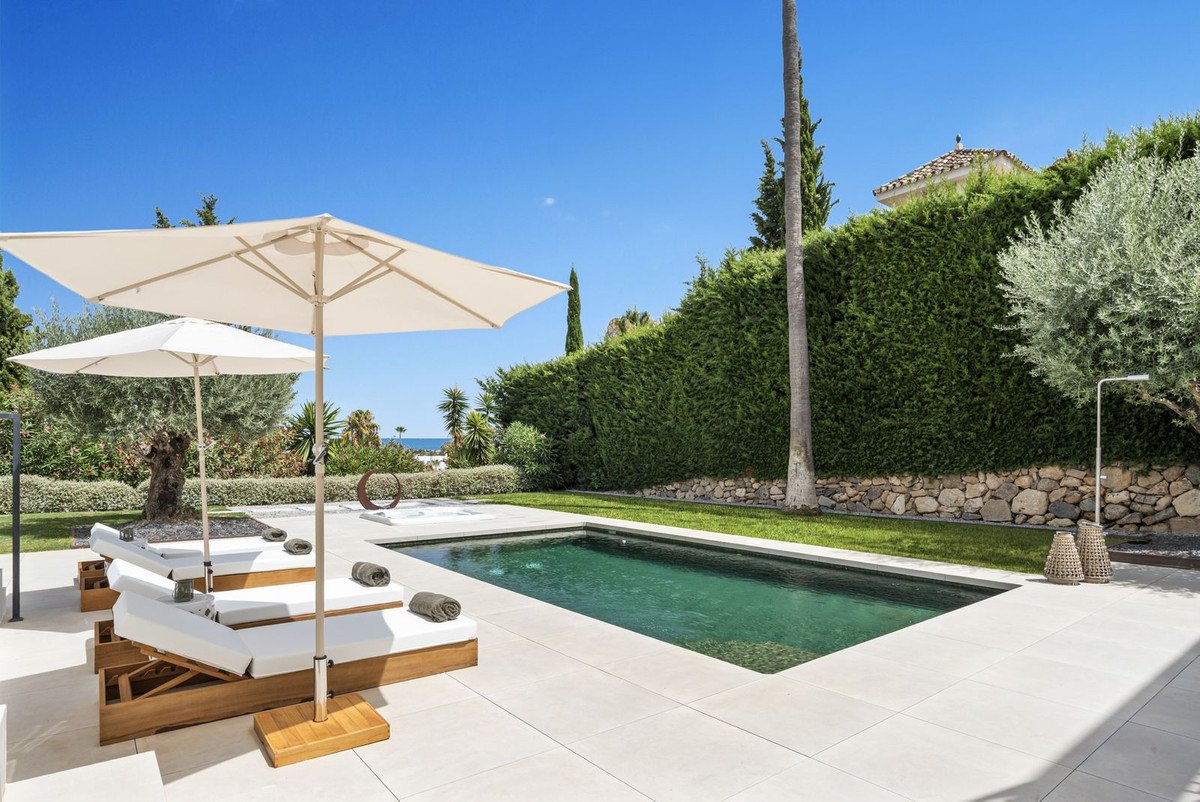 A refreshing swimming pool with loungers and umbrellas, overlooking a distant ocean view on a sunny day.