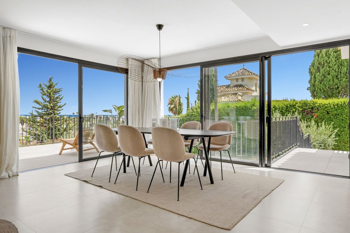 Modern dining room with a table and chairs, large windows opening to a terrace with sea and garden views.