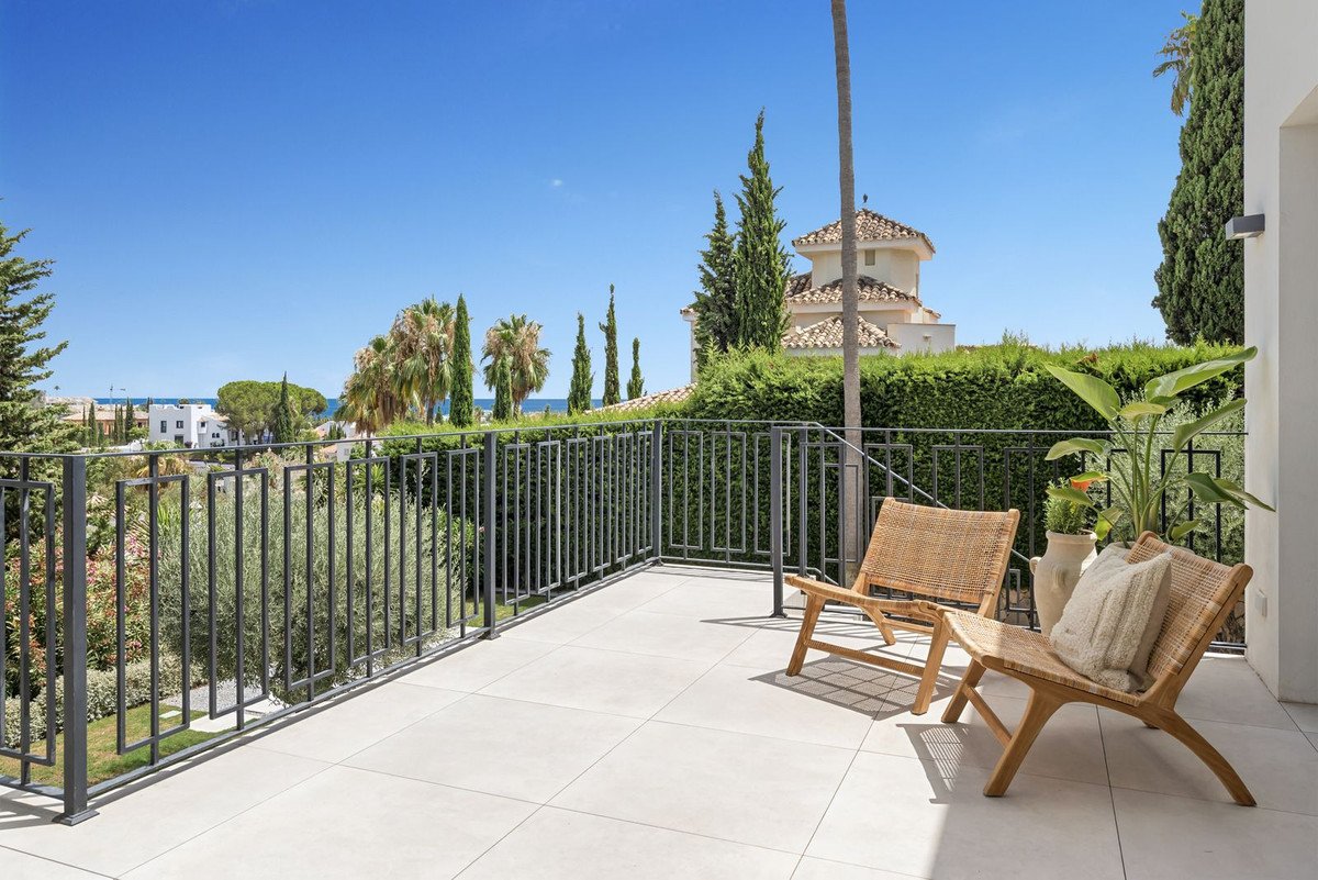 A spacious balcony with two rattan chairs and a distant sea view, surrounded by lush greenery.