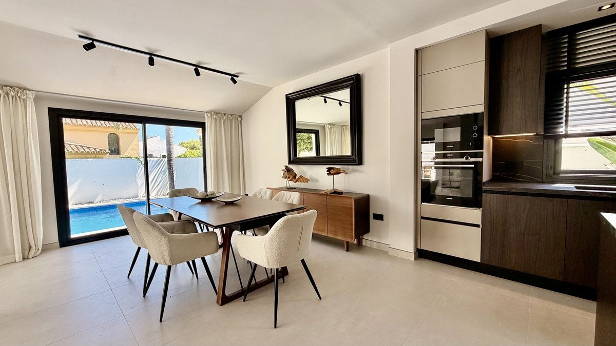 Modern dining area with pool view, adjacent to a contemporary kitchen with sleek cabinetry and appliances.