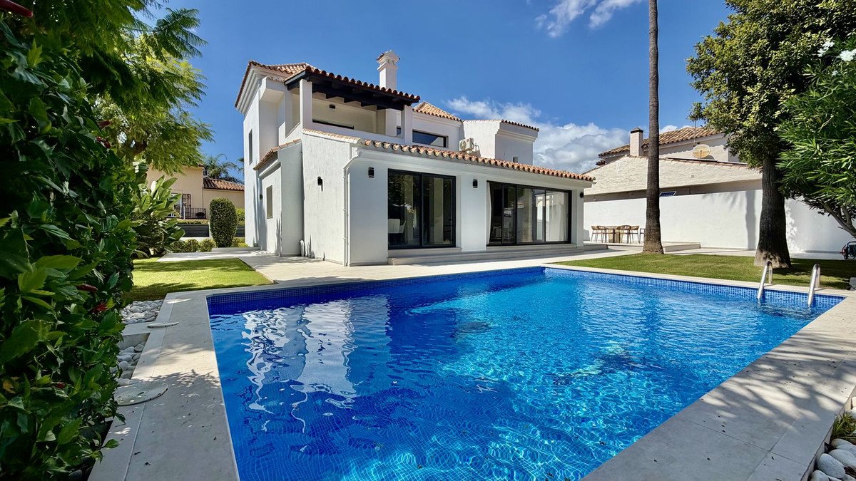 A modern white villa with a large blue swimming pool and a green lawn on a sunny day.
