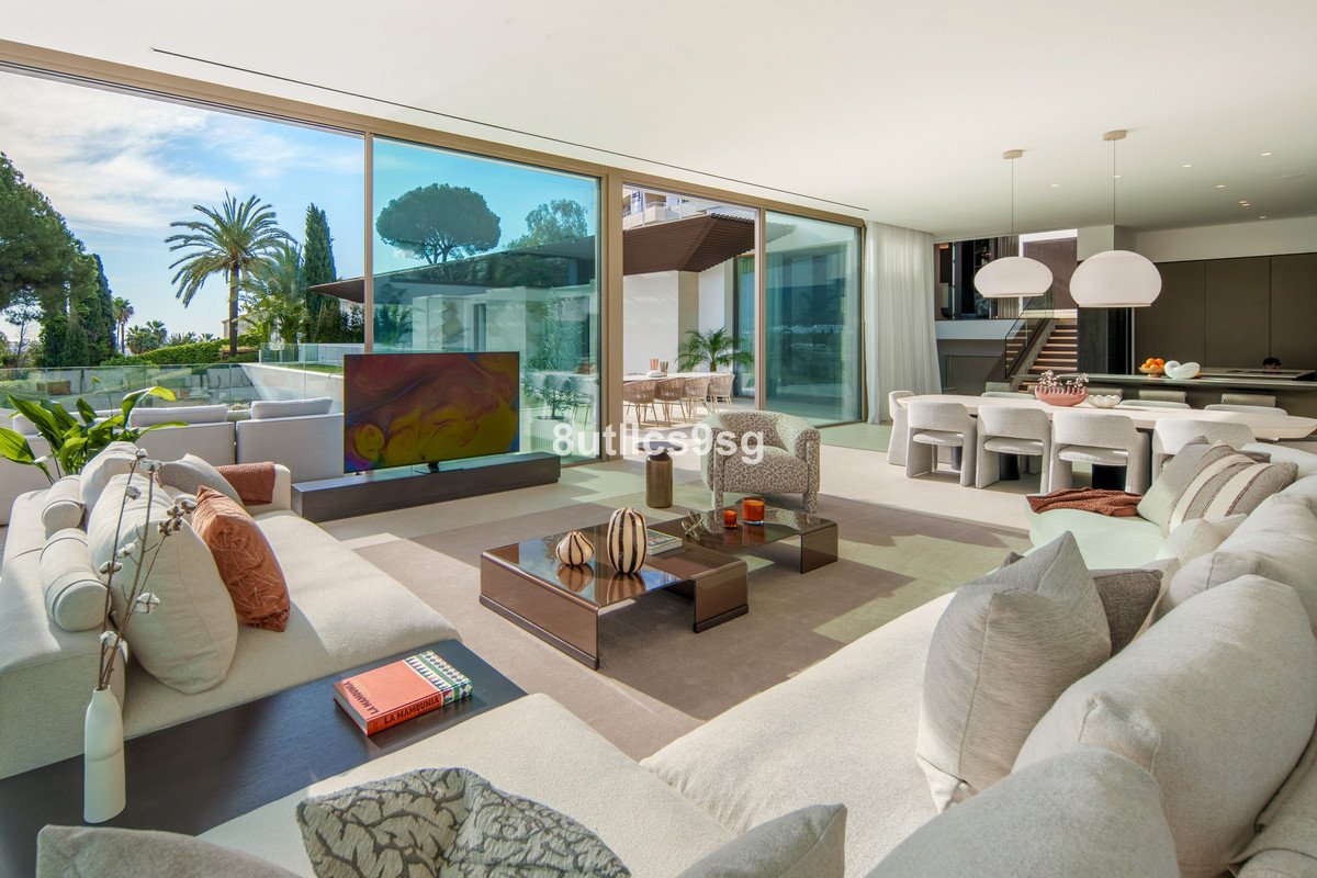 Spacious modern living room with a large sectional sofa, TV, dining area, and sliding glass doors opening to a sunny terrace and ocean view.