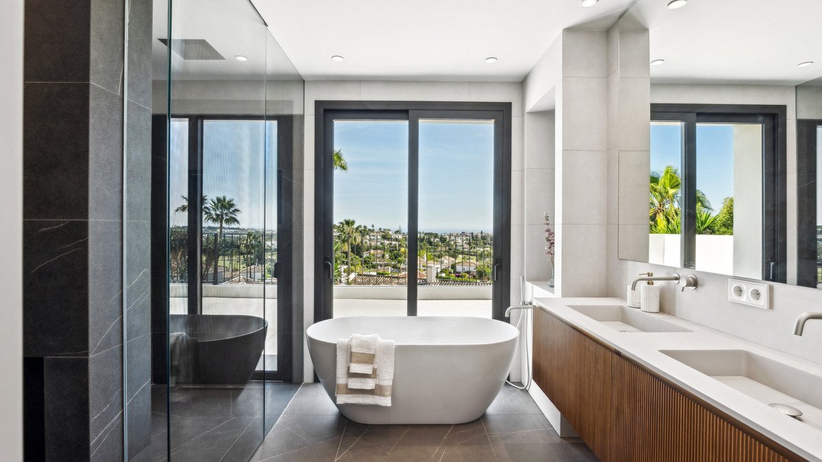 Modern bathroom with freestanding tub, double sinks, and ocean view through large windows