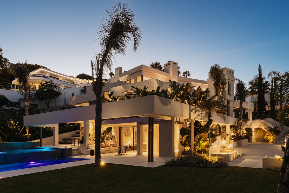 Modern villa with pool, terrace, and palm trees at night