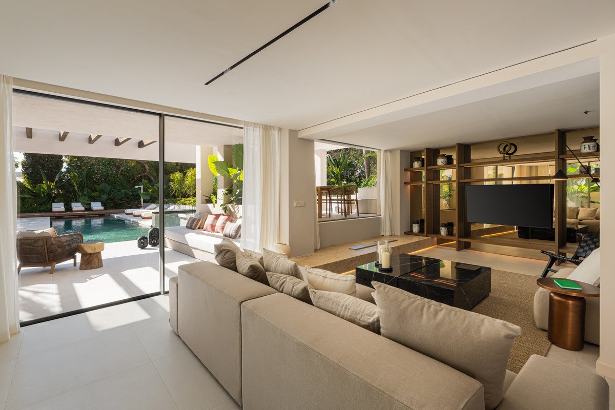 Modern living room with beige sofa, black coffee table, and sliding glass doors opening to a pool and outdoor seating area.