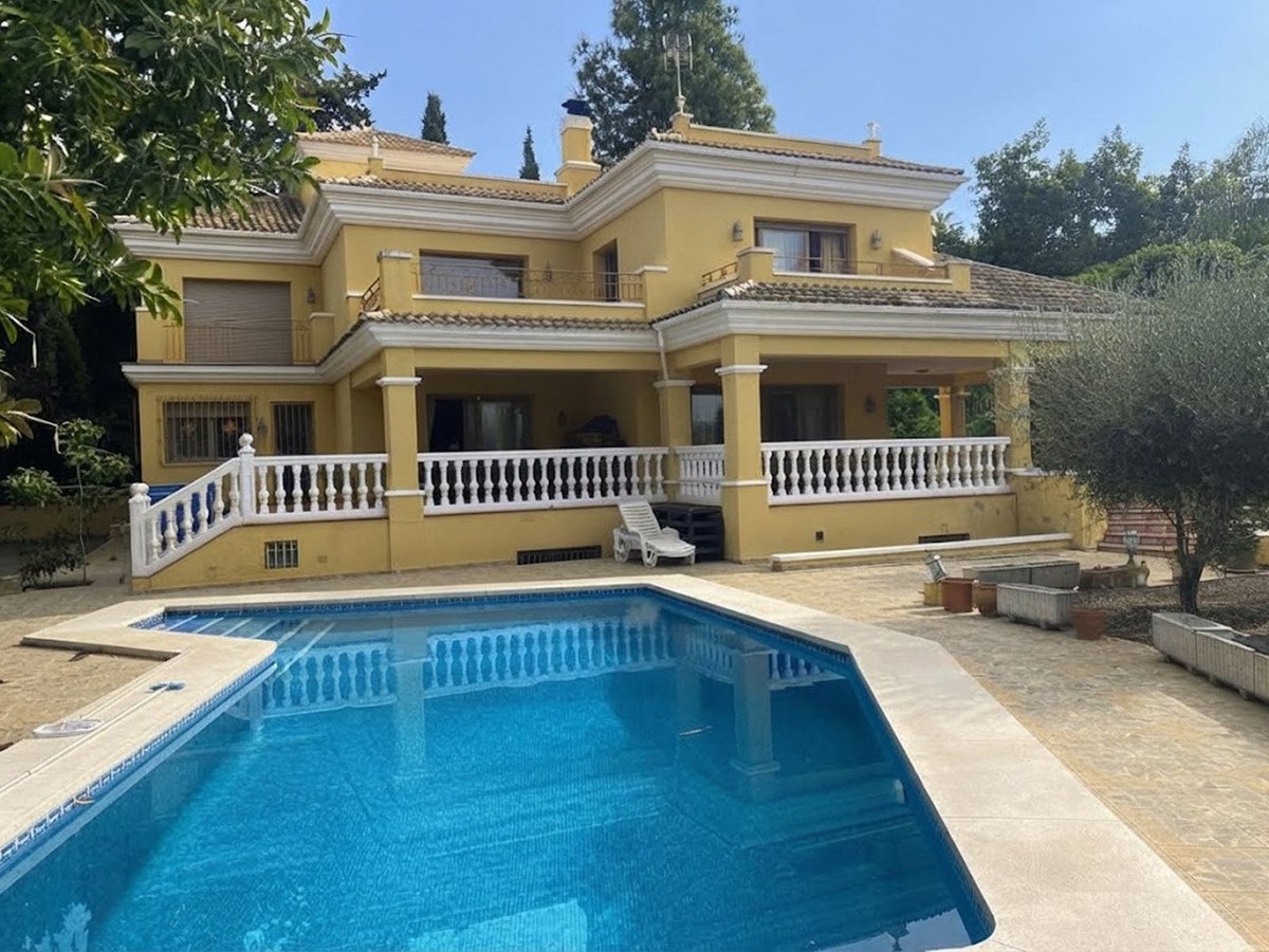 A yellow villa with a large blue swimming pool and a white-railed terrace on a sunny day.