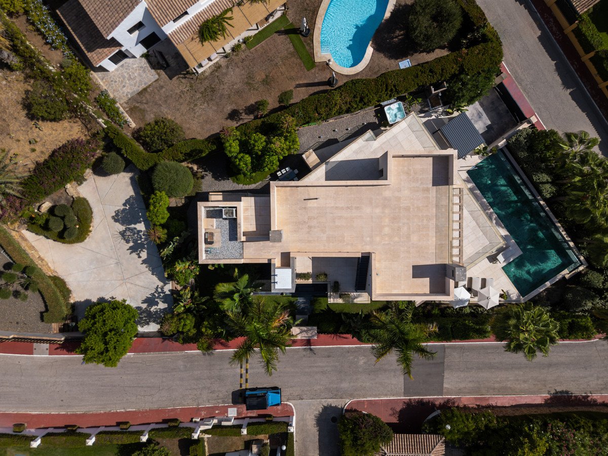 Aerial view of a modern villa featuring a large swimming pool, a jacuzzi, and lush green surroundings.