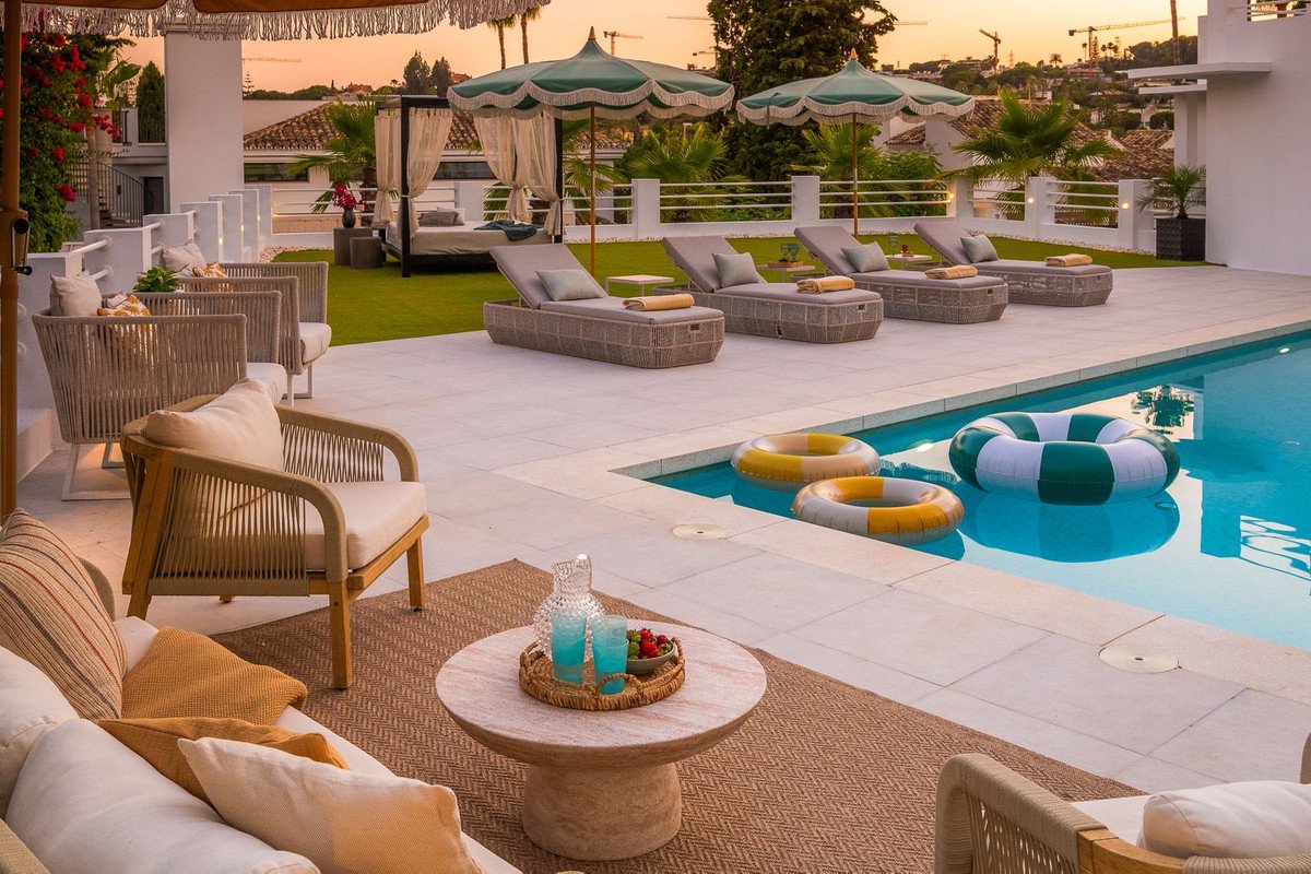 Outdoor lounge area with pool, sun loungers, and sunset view