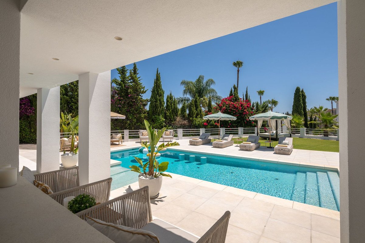 Luxury pool area with lounge chairs, umbrellas, and outdoor seating under a covered patio.