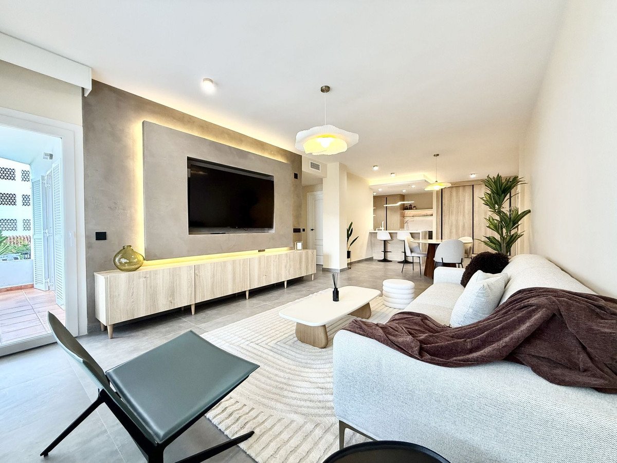 Modern living room with large TV, comfortable sofa, coffee table, and dining area in the background.