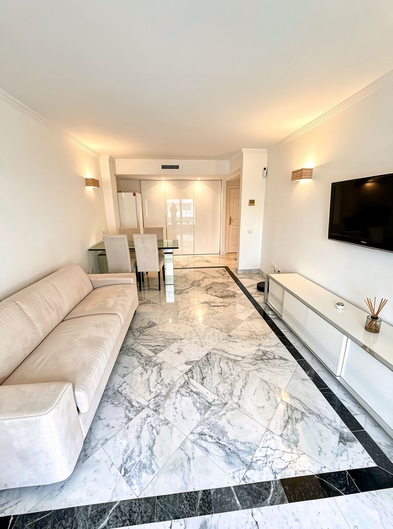 Modern living and dining area with marble floors, a plush sofa, dining set, and entertainment console.