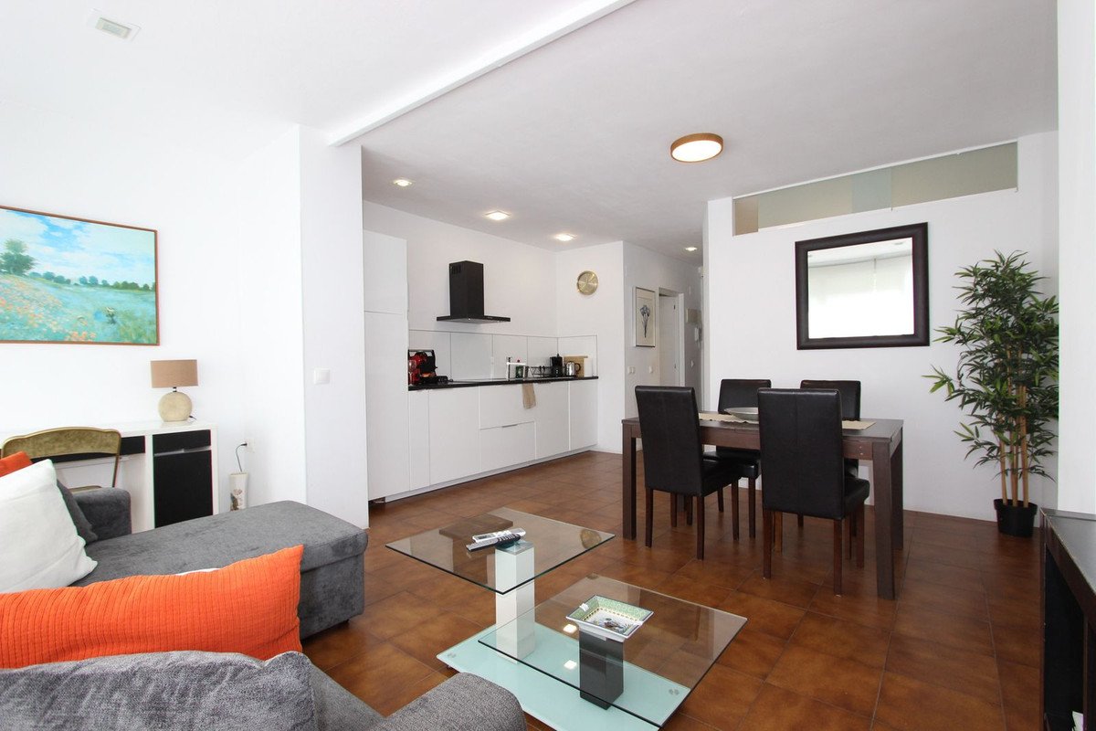 Modern open-plan living and dining area with grey sofa, glass coffee table, and kitchen in background