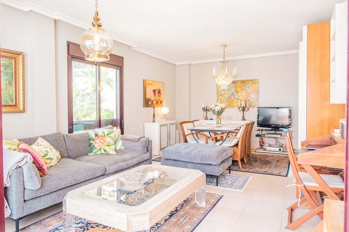 Comfortable living and dining room with a grey sofa, ottoman, dining table, and television, TV, overlooking a garden view.