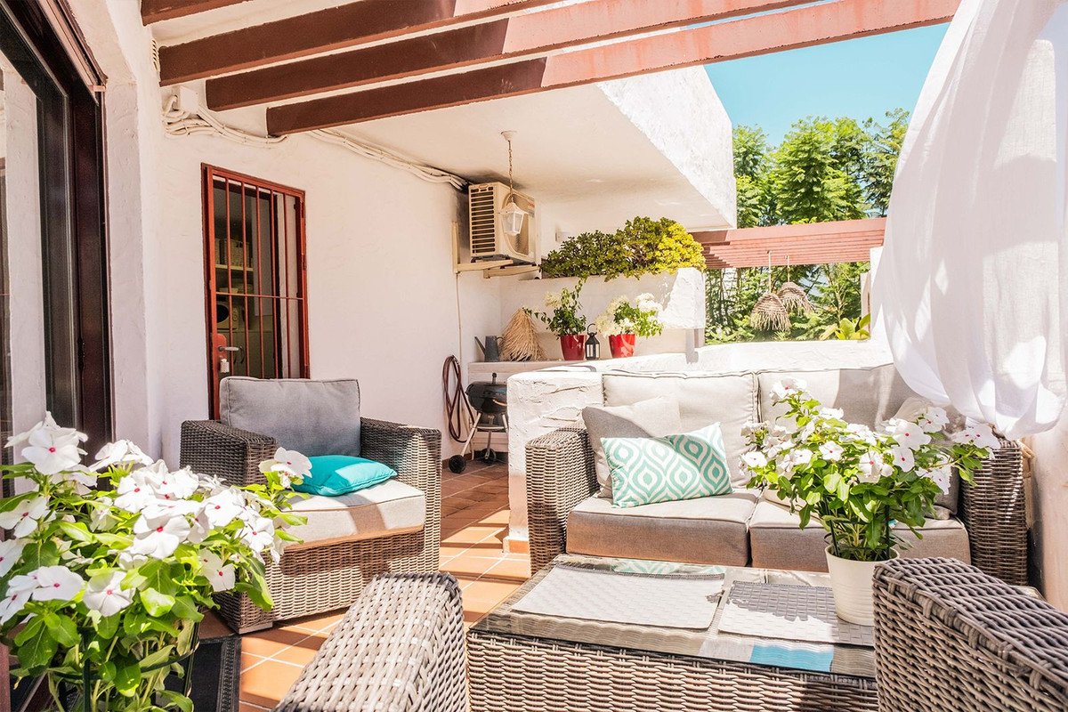 Covered terrace with comfortable outdoor seating, coffee table, lush plants, and a view of greenery.