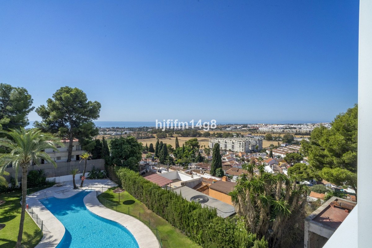 Panoramic view of a town with a swimming pool and the sea in the distance under a clear blue sky.