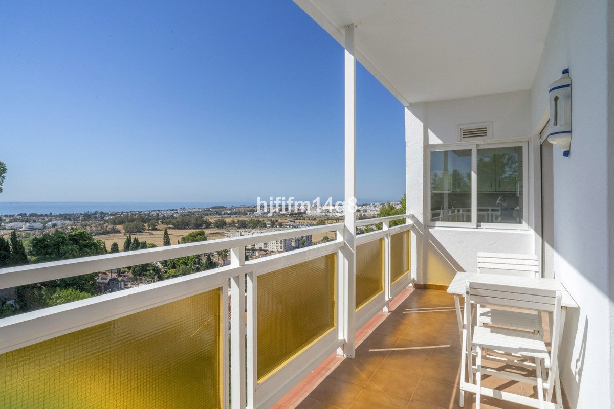 A sunny balcony with a table and chairs offering a panoramic view of the sea and landscape.
