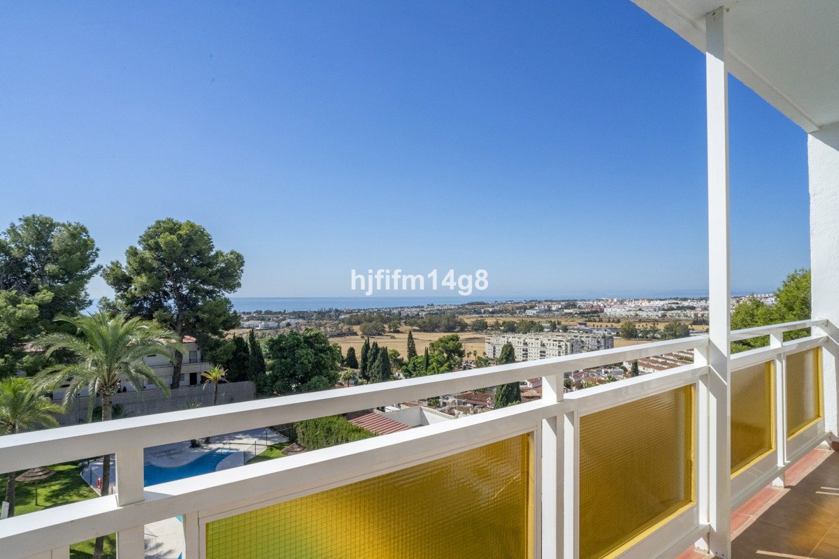 View from a balcony overlooking a town, with the sea in the distance and a swimming pool below.