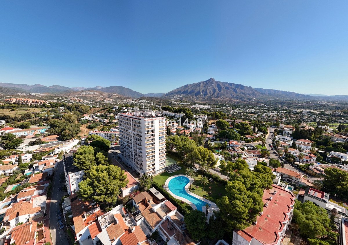 Aerial view of a tall apartment building with a swimming pool in the foreground and mountains in the background.