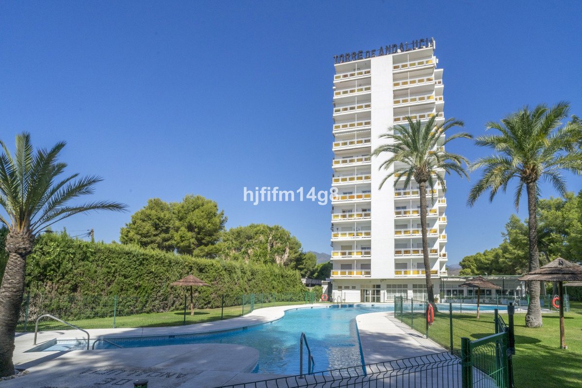 A tall white building with balconies, surrounded by palm trees and a swimming pool.