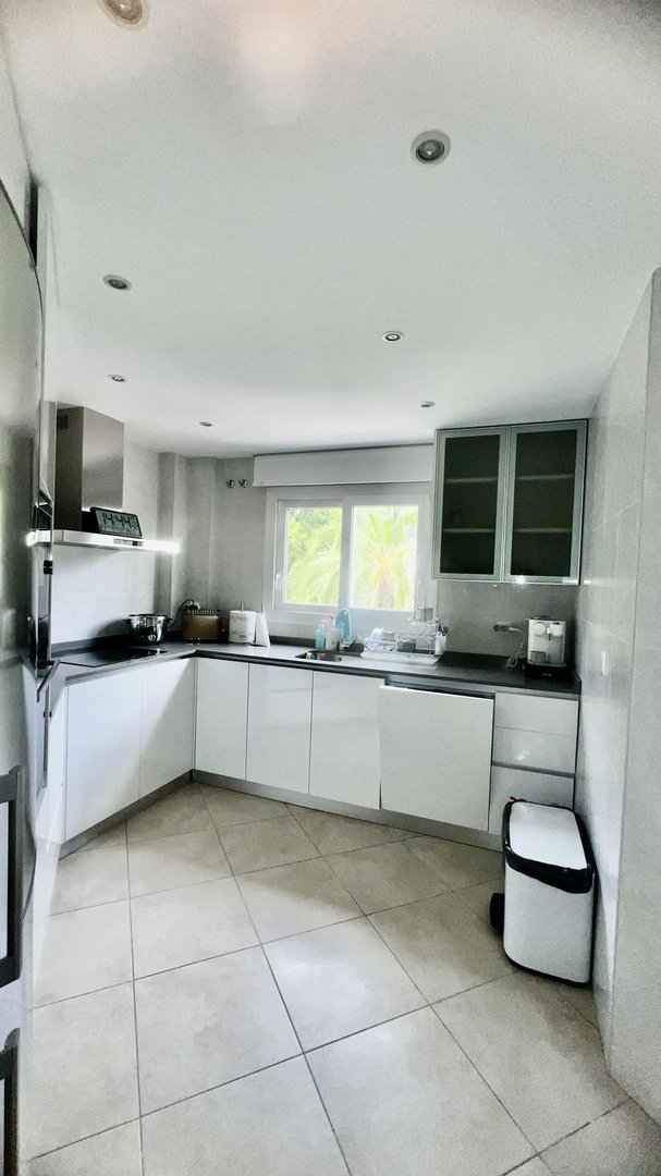 Modern kitchen with white cabinets, tiled floor, and a window showing greenery outside.