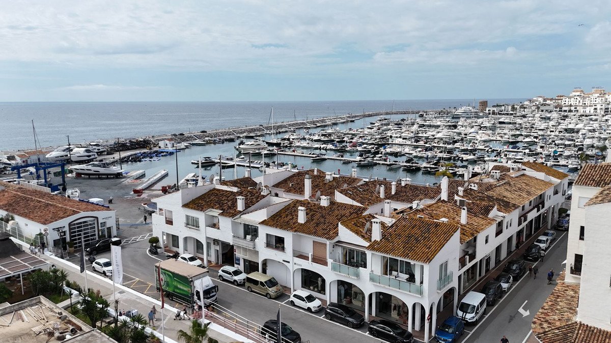 View of a marina filled with boats, overlooking white townhouses with terracotta roofs and the blue sea.